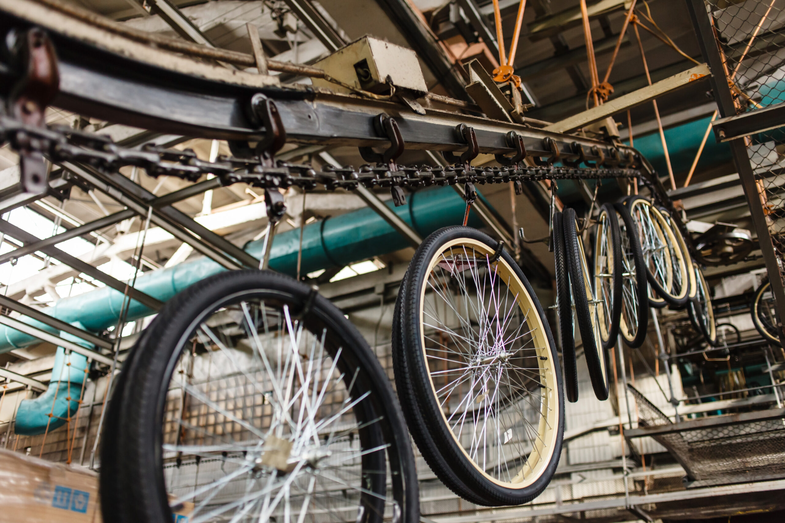 Bicycles hanging from a ceiling rack in a warehouse-like bike storage area, with chains and metal framework visible above ground.