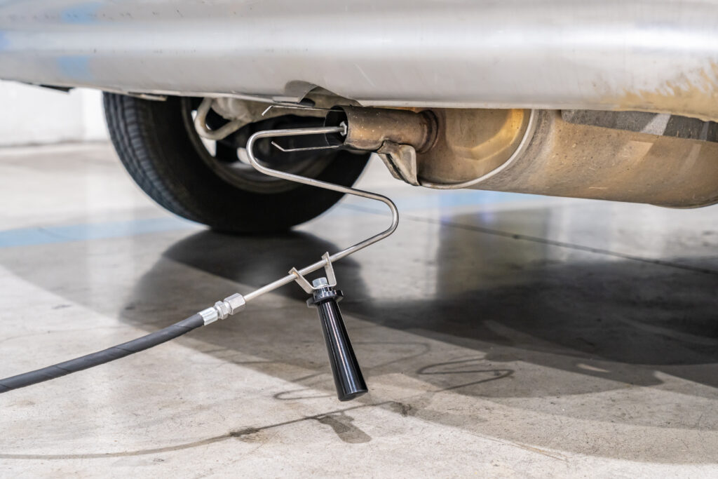 Underbelly of a car showing the exhaust pipe with a diagnostic probe inserted and cables hanging below.