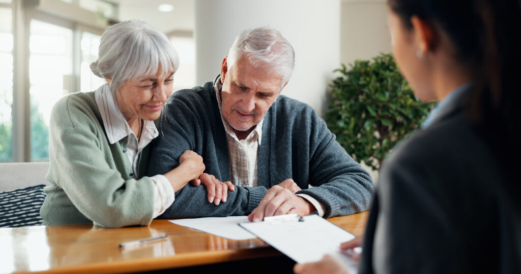 Older couple studies documents at a table with a professional advisor nearby.