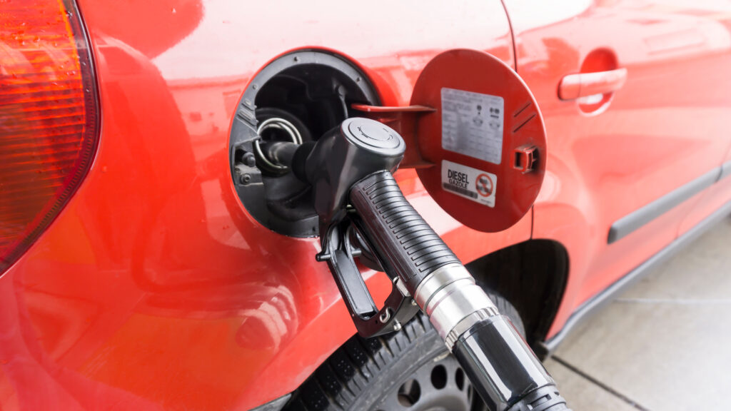 Close-up of a diesel fuel nozzle inserted into a red car's fuel filler, with the cap cover open