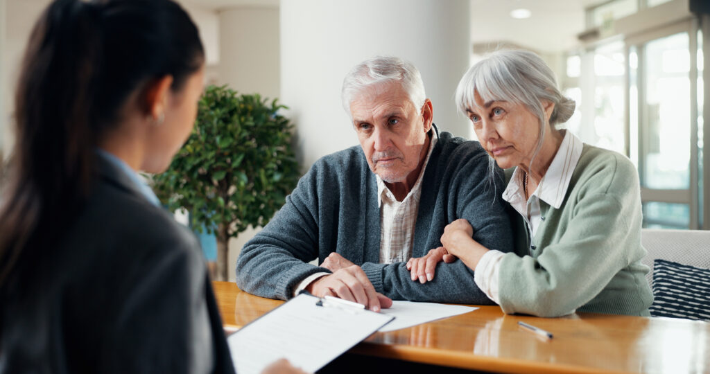 Older couple consults with a professional at a table in a bright office, papers in front of them.