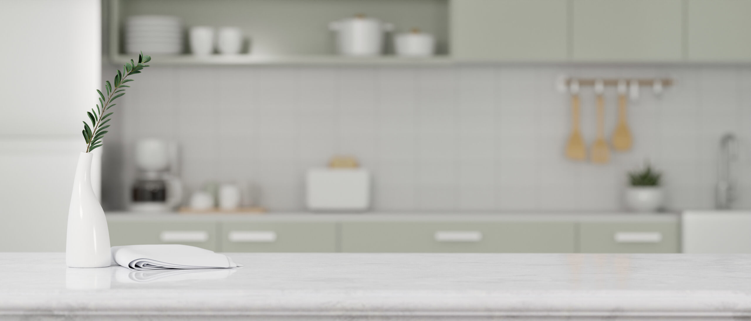 White vase with a green sprig on a marble kitchen island, with a blurred pastel-green kitchen in the background.