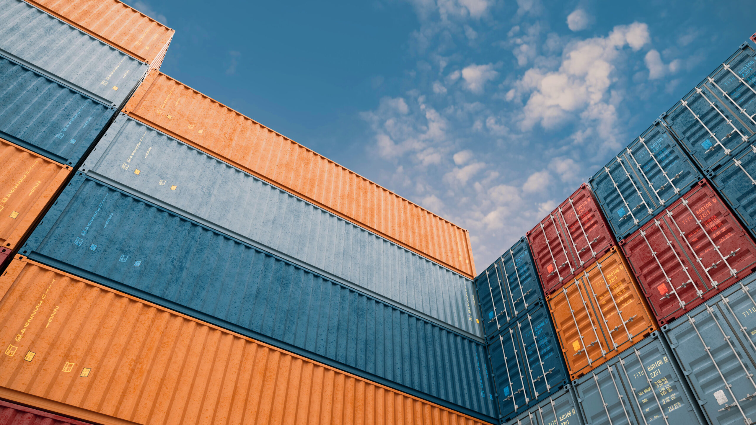 Colorful shipping containers stacked against a blue sky, viewed from a diagonal angle.
