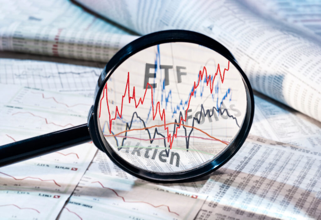 Close-up of a magnifying glass over stock charts with red and blue trend lines and the letters ETF visible, signaling financial analysis of funds.