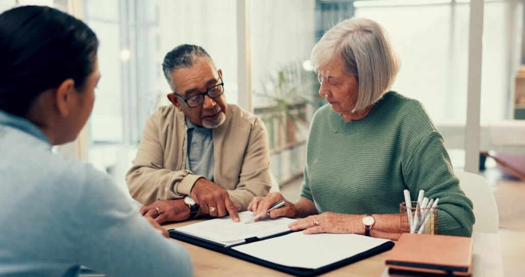 Three adults seated at a table in a bright office, reviewing documents together.