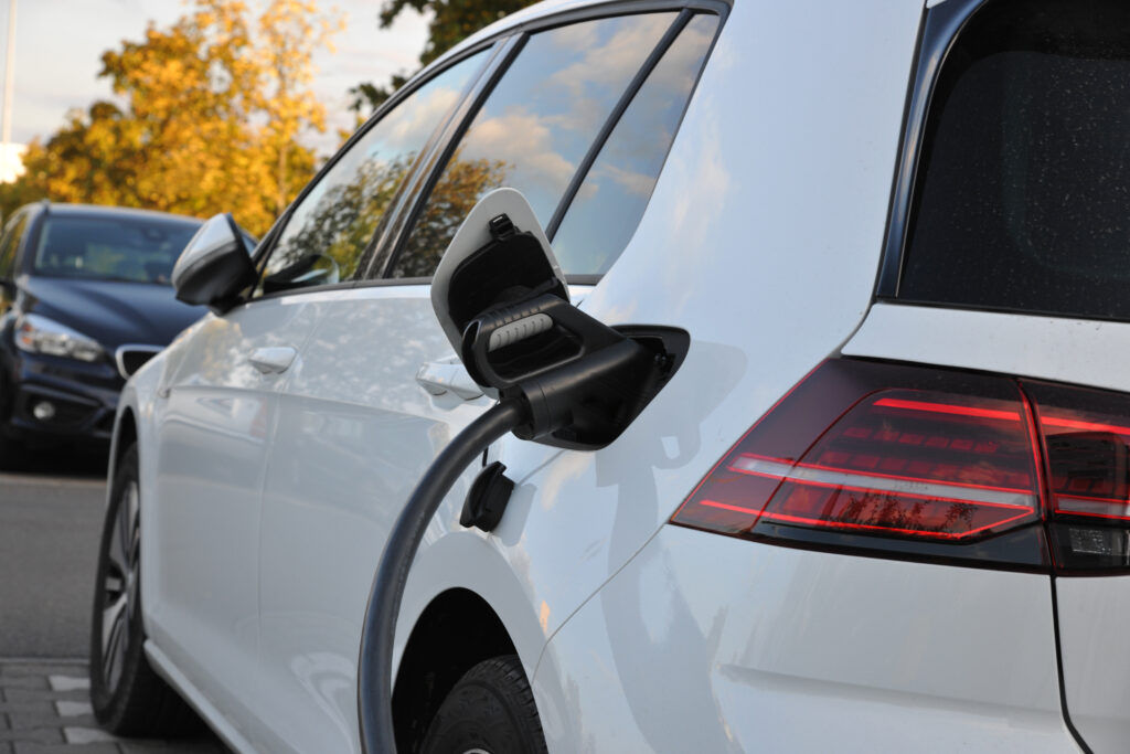 Close-up of a white electric SUV with the charging port open and a charging cable plugged in.