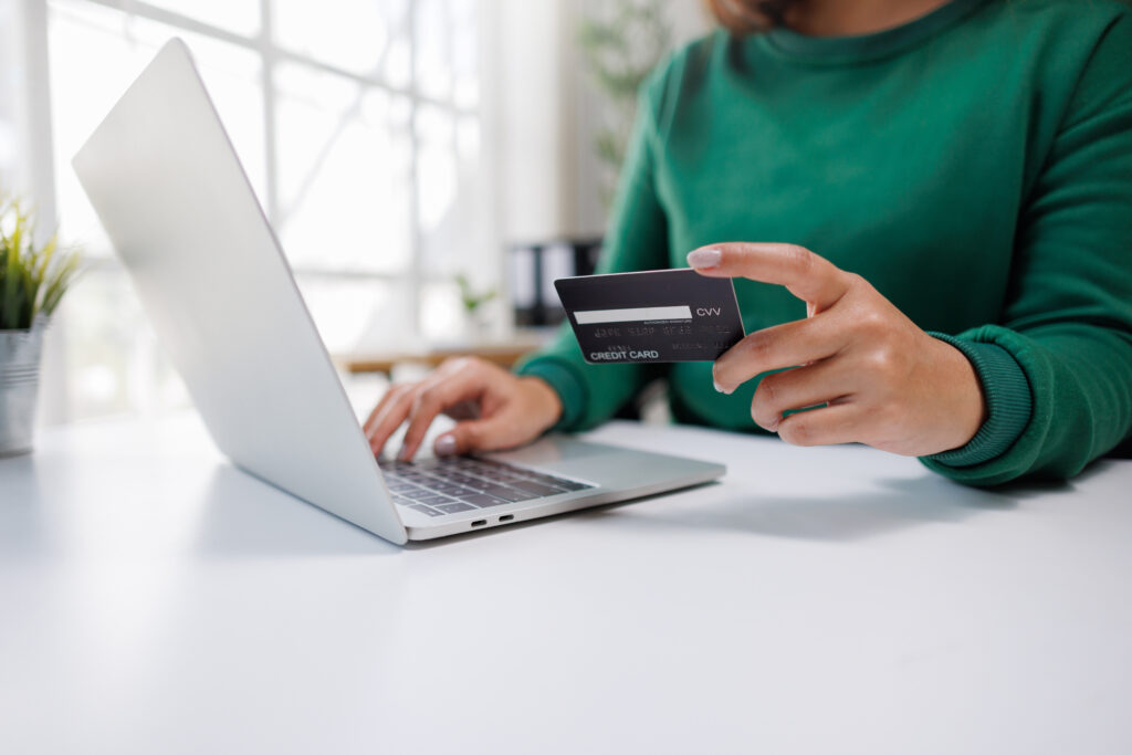 Person in a green shirt typing on a laptop while holding a credit card, suggesting online shopping or checkout.