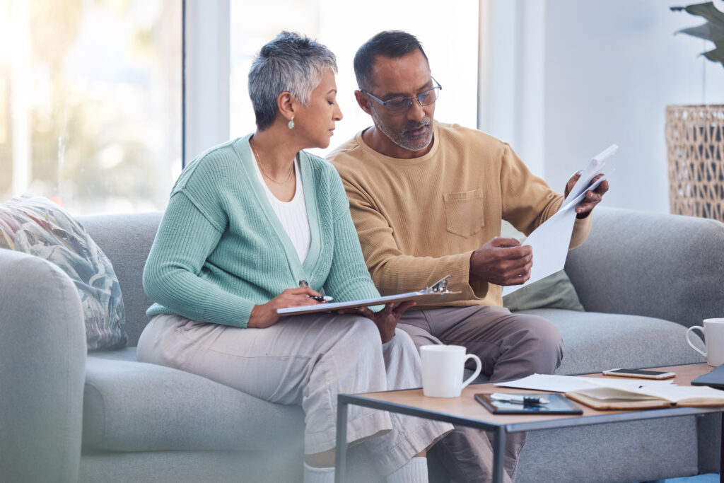 Two adults sit on a couch reviewing documents together in a bright living room with coffee mugs on the table nearby.