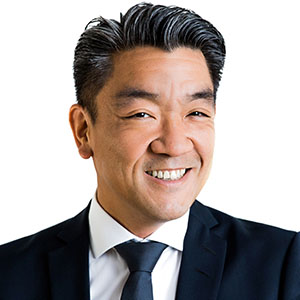 Smiling Asian man in a dark suit and tie, head-and-shoulders portrait.