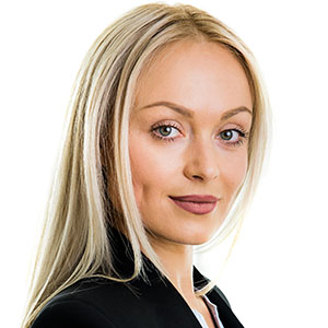 Professional headshot of a blonde woman in a black blazer, looking at the camera with a slight smile.