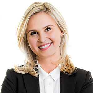 Portrait of a smiling blonde woman in a black blazer and white shirt, looking at the camera.