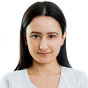 Portrait of a woman with dark hair, facing the camera in a light-colored top against a white background, neutral expression.